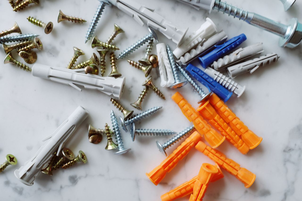 Ensemble de chevilles en plastique multicolores accompagnées de vis métalliques variées de tailles différentes, disposées sur une table en marbre blanc dans un atelier moderne